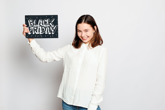 Shopping, vente au détail, vendredi noir, vente, shopping et concept de personnes - Jeune fille brune souriante tient une pancarte du vendredi noir. Vente du vendredi noir.