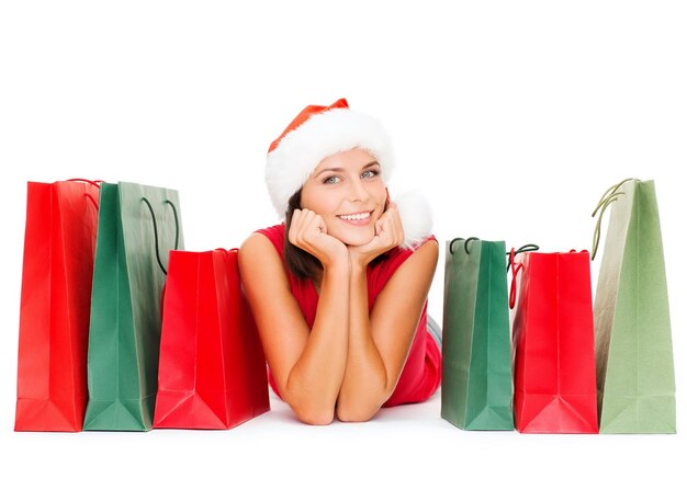 shopping, vente, cadeaux, noël, concept de noël - femme souriante en chemise rouge et bonnet de noel avec des sacs à provisions