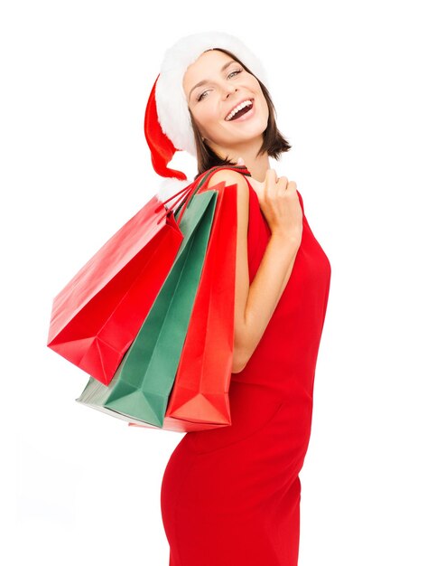 shopping, vente, cadeaux, noël, concept de noël - femme souriante en robe rouge et bonnet de noel avec des sacs à provisions