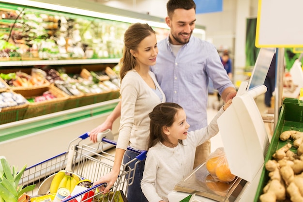 shopping, vente, consumérisme et concept humain - famille heureuse avec enfant pesant des oranges à l'échelle à l'épicerie