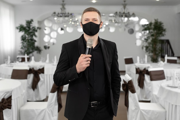 Showman en costume et masque de protection avec un microphone dans les mains dans la salle de banquet de rastoran