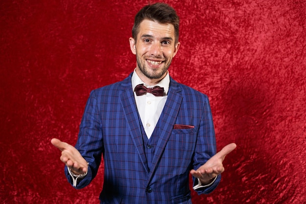 Showman joyeux en costume bleu élégant et noeud papillon montrant un geste de bienvenue avec les mains