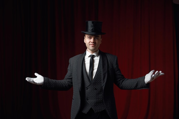 Showman à la mode souriant ou illusionniste en manteau et chapeau haut sur scène