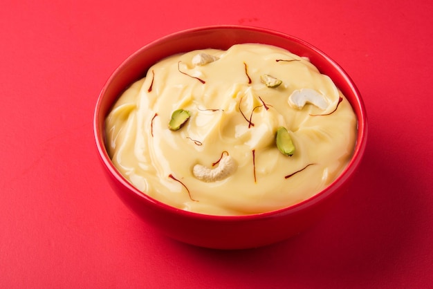 Le Shrikhand est un plat indien sucré à base de yaourt égoutté, garni de fruits secs et de safran. Servi dans un bol en céramique. Isolé sur fond coloré ou en bois. Mise au point sélective