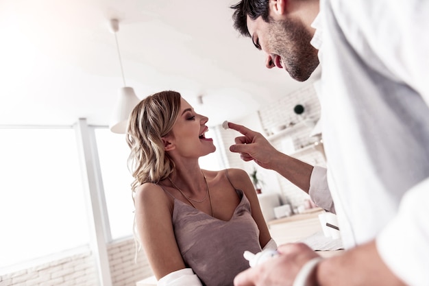 Si amusant. Jolie jeune femme aux cheveux longs portant de beaux vêtements maison se sentir magnifique tout en s'amusant avec son mari