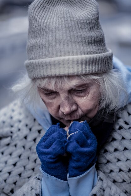 Photo si froid. femme sans-abri déprimée essayant de se réchauffer les mains tout en étant à l'extérieur