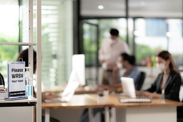 Signalisation de désinfectant pour les mains autour du bureau pour les pratiques d'hygiène après la réouverture. les gens d'affaires travaillent et portent un masque facial dans un nouveau bureau normal pour empêcher la propagation du virus covid-19