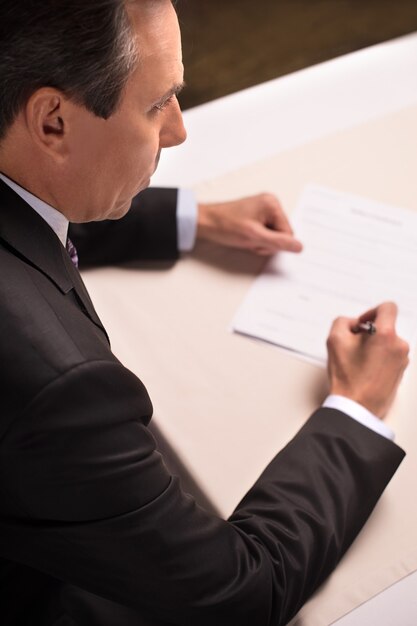 Signature d'un contrat. Vue de dessus d'un homme mûr en tenue de soirée signant un document