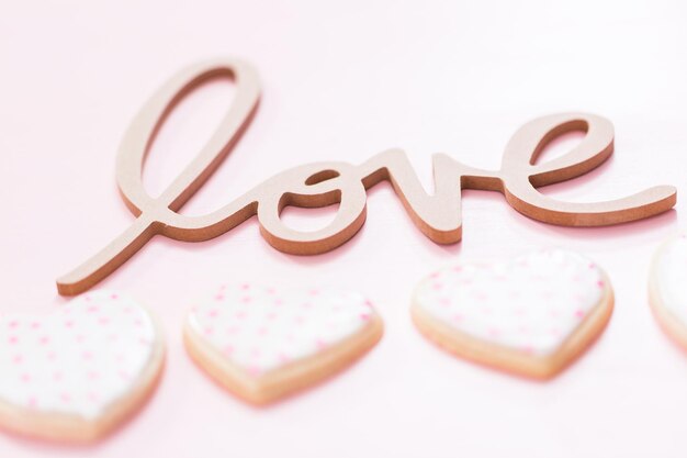 Signe d'AMOUR avec des biscuits au sucre en forme de coeur sur fond rose.