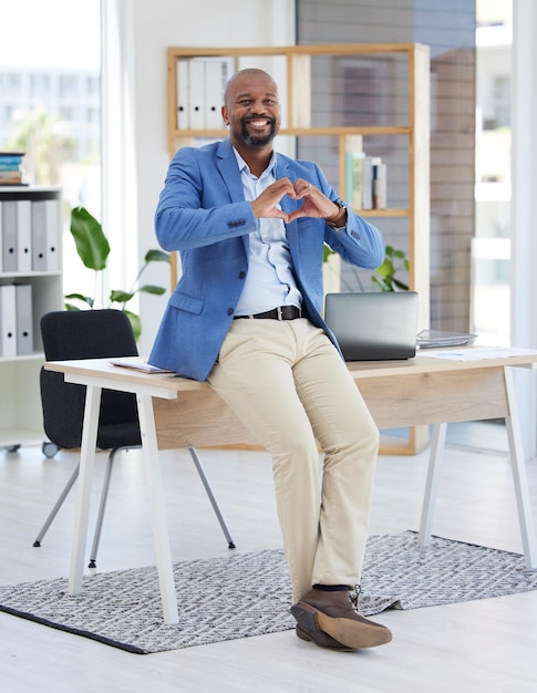 Signe de coeur d'homme d'affaires africain ou bureau pour le bonheur de sourire ou assis sur le bureau avec amour