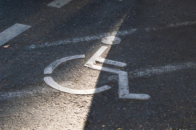 Signe de fauteuil roulant sur un parking asphalté indiquant une place réservée aux personnes handicapées physiques