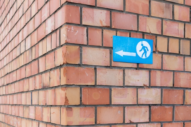 Un signe avec un signe de flèche et un homme en cours d'exécution vissé à un mur de briques. Le signe indique le coin d'un bâtiment en brique.