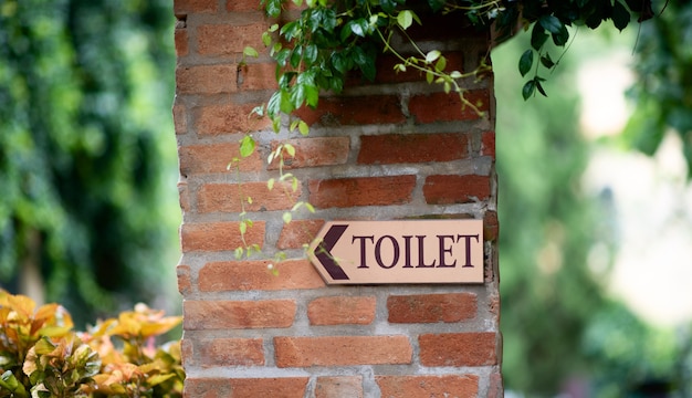 Signe de toilettes sur le mur de briques rouges avec des feuilles