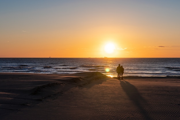 Silhouete d'une paire amoureuse. Beau paysage coucher de soleil à la mer du Nord avec un ciel orange et une réflexion dorée impressionnante sur les vagues du soleil. Incroyable vue du coucher de soleil d'été sur la plage.