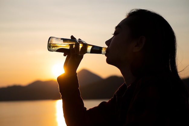 Silhouette asiatique femme buvant de l'eau sur la plage au crépuscule