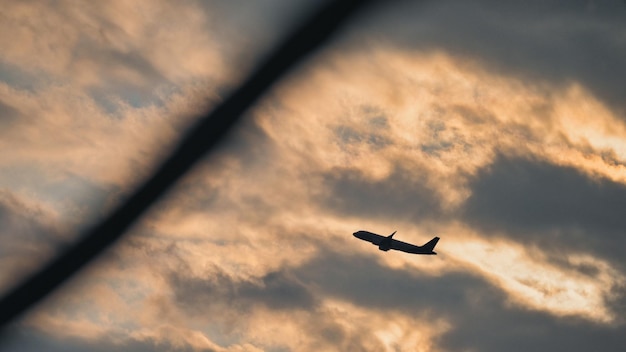 Silhouette d'un avion volant dans le ciel nuageux au coucher du soleil