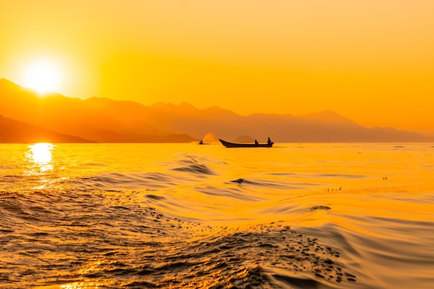 Silhouette d'un bateau de pêche avec un pêcheur pêchant dans le coucher de soleil orange du lac Shkoder à Shiroka Albanie