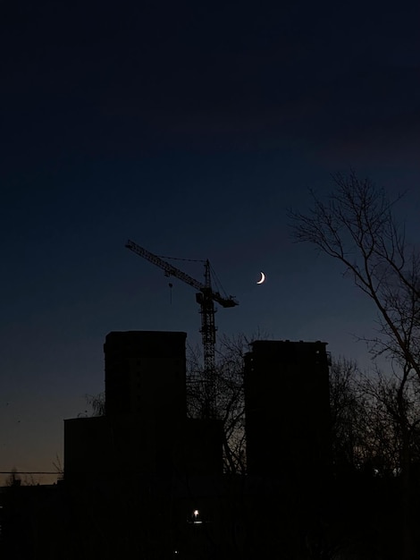 Photo silhouette d'un bâtiment avec une grue et un croissant de lune