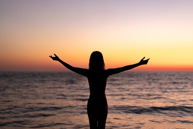 Silhouette de la belle jeune femme pensive gracile avec un sentiment de liberté monter la main sur un beau coucher de soleil