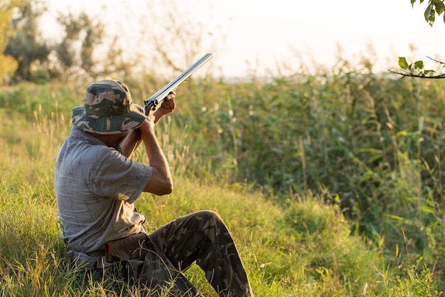 Silhouette d'un chasseur avec une arme à feu dans les roseaux contre le soleil, une embuscade pour les canards avec des chiens