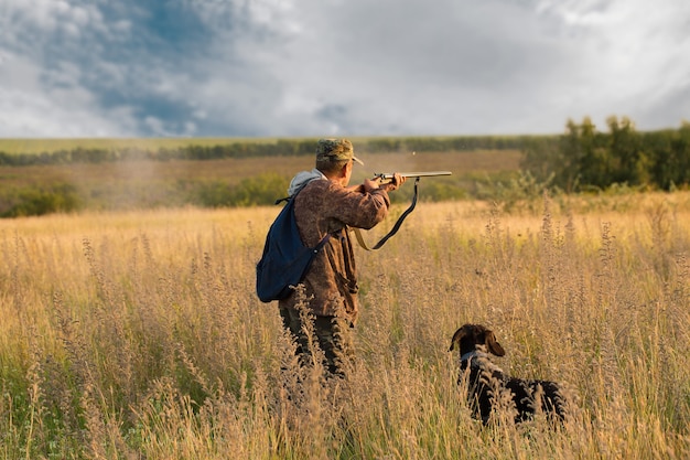 Silhouette d'un chasseur avec une arme à feu dans les roseaux contre le soleil, une embuscade pour les canards avec des chiens