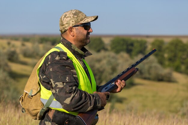 Silhouette d'un chasseur avec une arme à feu dans les roseaux contre le soleil, une embuscade pour les canards avec des chiens