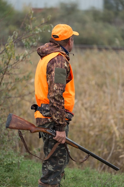 Silhouette d'un chasseur avec une arme à feu dans les roseaux contre le soleil une embuscade pour des canards avec des chiens