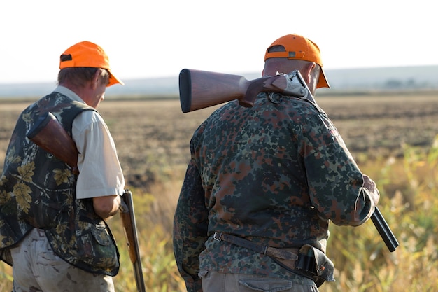 Silhouette d'un chasseur avec une arme à feu dans les roseaux contre le soleil une embuscade pour des canards avec des chiens