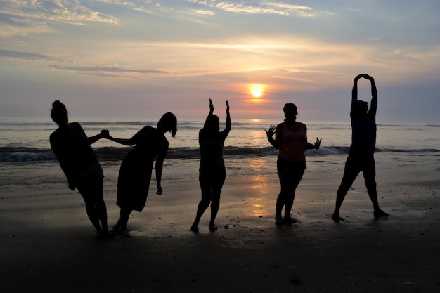 Silhouette de cinq personnes jouant au bord de la mer au coucher du soleil Golden hour