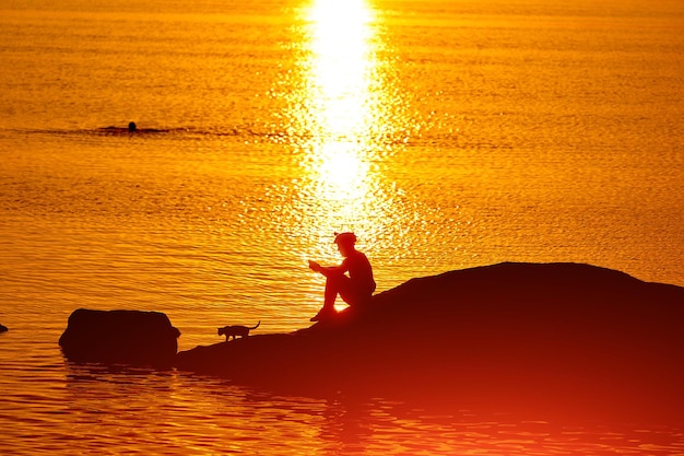 Silhouette coucher de soleil d'un homme assis sur un lac Soleil orange extérieur d'un homme se reposant