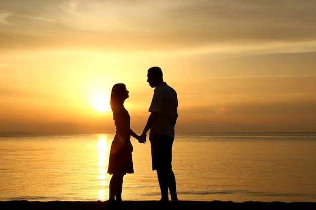 Silhouette d'un couple d'amoureux heureux au coucher du soleil au bord de la mer