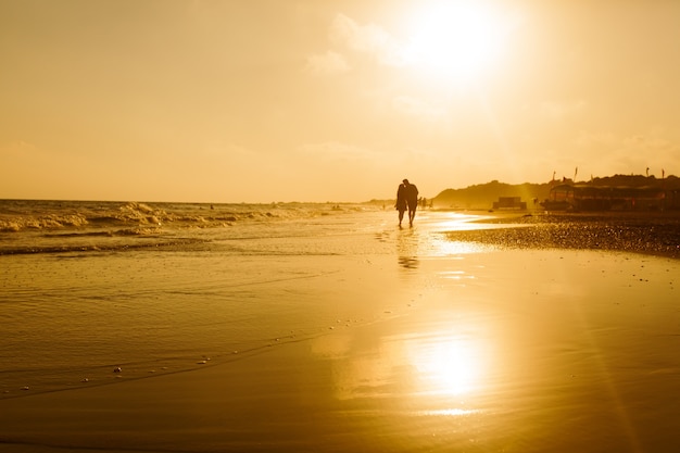 Silhouette d'un couple d'amoureux qui marche le long d'une plage de sable et profite du coucher du soleil