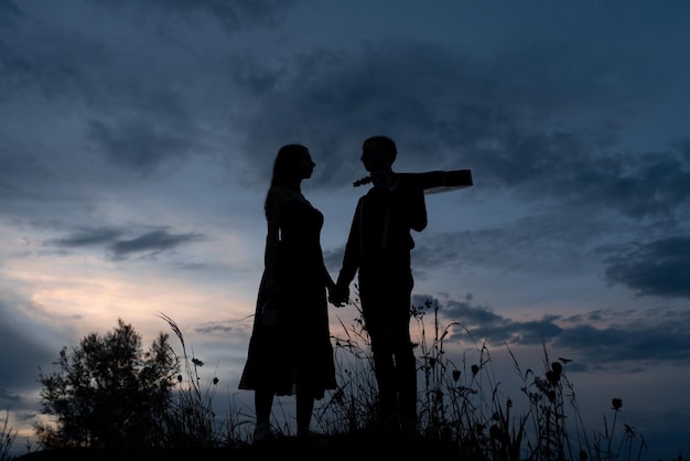 Silhouette d'un couple amoureux à un rendez-vous L'homme tient la main de la fille Le mec aux crabes a une guitare Filmé au coucher du soleil