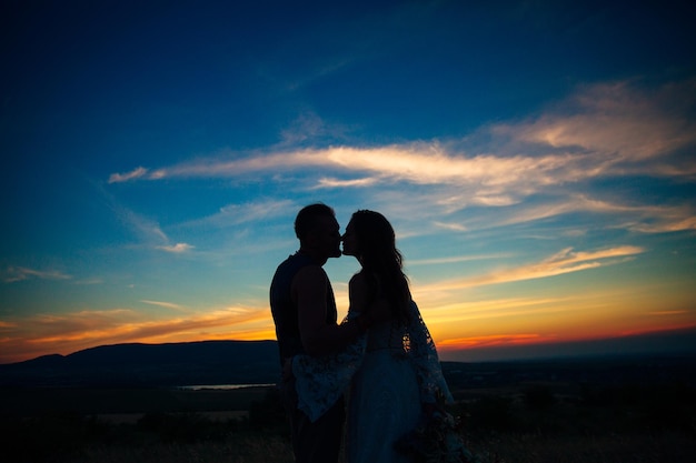 Silhouette d'un couple étreignant et embrassant au coucher du soleil sur fond de montagnes et de mer