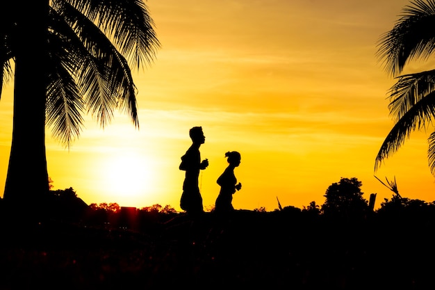 Silhouette de couple, faire du jogging dans le parc au coucher du soleil.