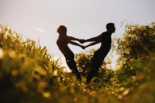 Silhouette de couple faisant des exercices de yoga en plein air dans le parc