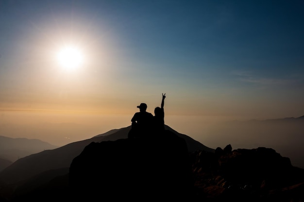 silhouette d'un couple de personnes assises sur une montagne en regardant le coucher du soleil