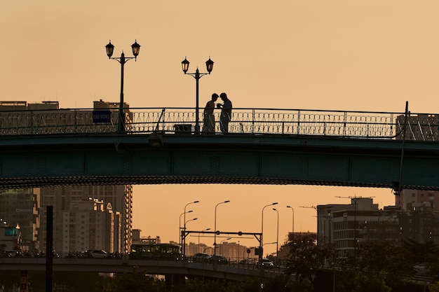 Photo silhouette d'un couple romantique marchant main dans la main sur le pont le soir beau ciel