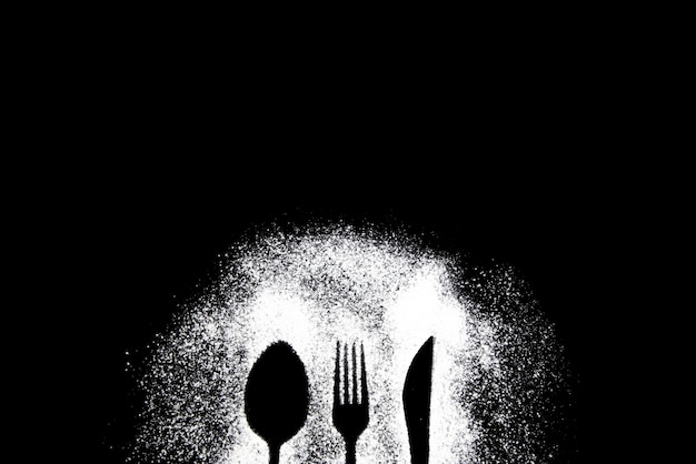 Silhouette d'un couteau, d'une fourchette et d'une cuillère saupoudrés de farine sur un fond sombre avec espace de copie