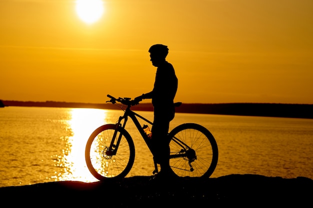 Silhouette d'un cycliste avec casque au coucher du soleil près de la rivière