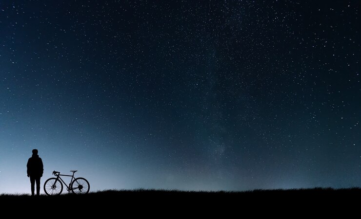 Silhouette d'un cycliste avec un vélo debout à proximité au ciel étoilé.