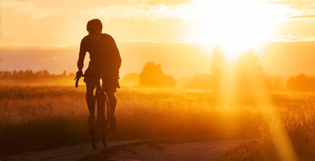 Silhouette d'un cycliste sur un vélo de gravier sur un sentier dans un champ sur un coucher de soleil spectaculaire