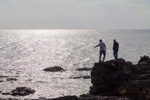 Silhouette de deux hommes debout sur un gros rocher au bord de l'océan. Lanzarote, Espagne.