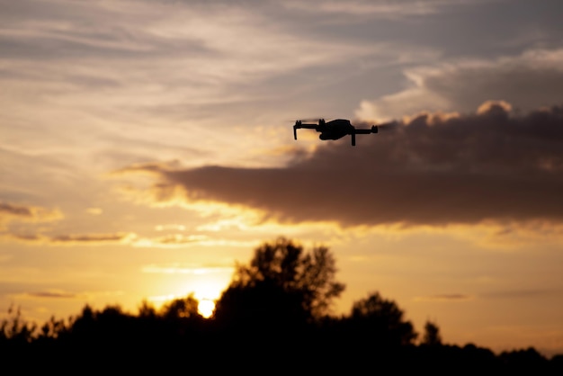 Silhouette de drone volant dans le ciel et filmant le coucher du soleil. Petit avion portable en vol