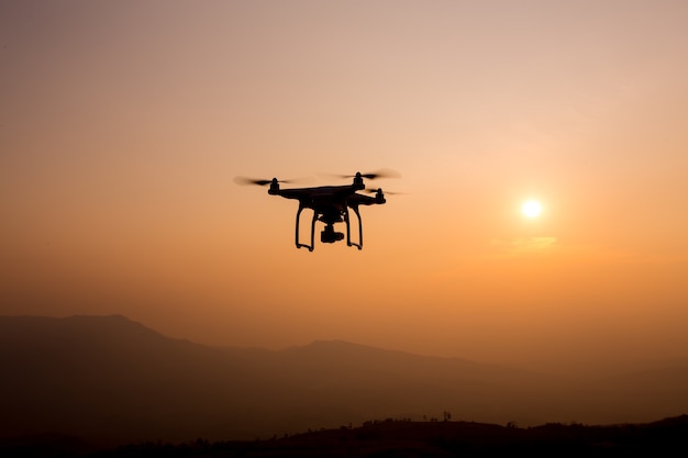 Silhouette de drone volant dans le paysage du coucher du soleil avec appareil photo numérique au coucher du soleil prêt à voler.