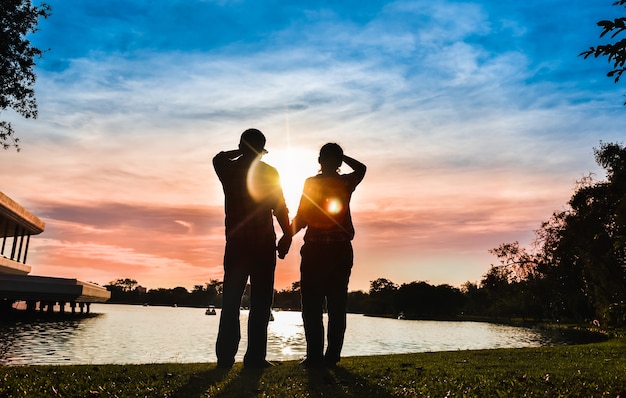 La silhouette du couple se tient par la main et en regardant le coucher de soleil coloré ensemble