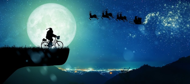 Silhouette du Père Noël à cheval sur son vélo au cours de la pleine lune