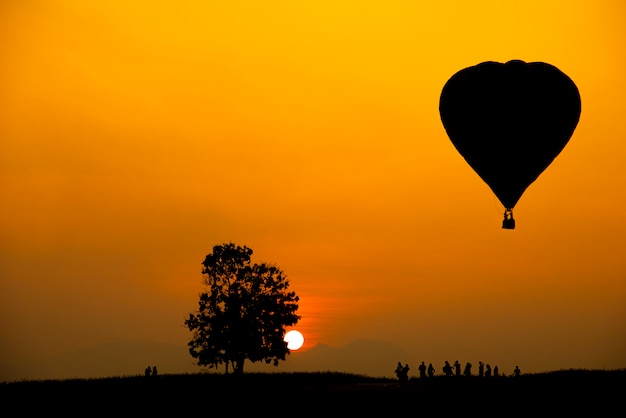 Silhouette du peuple, arbre et montgolfière sur un coucher de soleil coloré avec grand soleil.