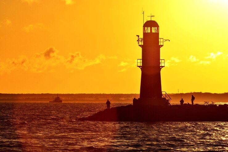 Photo silhouette du phare par la mer contre le ciel au coucher du soleil