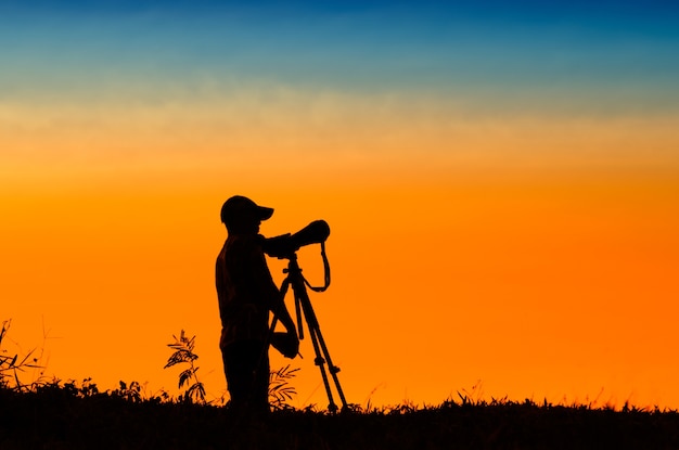 silhouette du photographe prenant la photo du paysage pendant le coucher du soleil